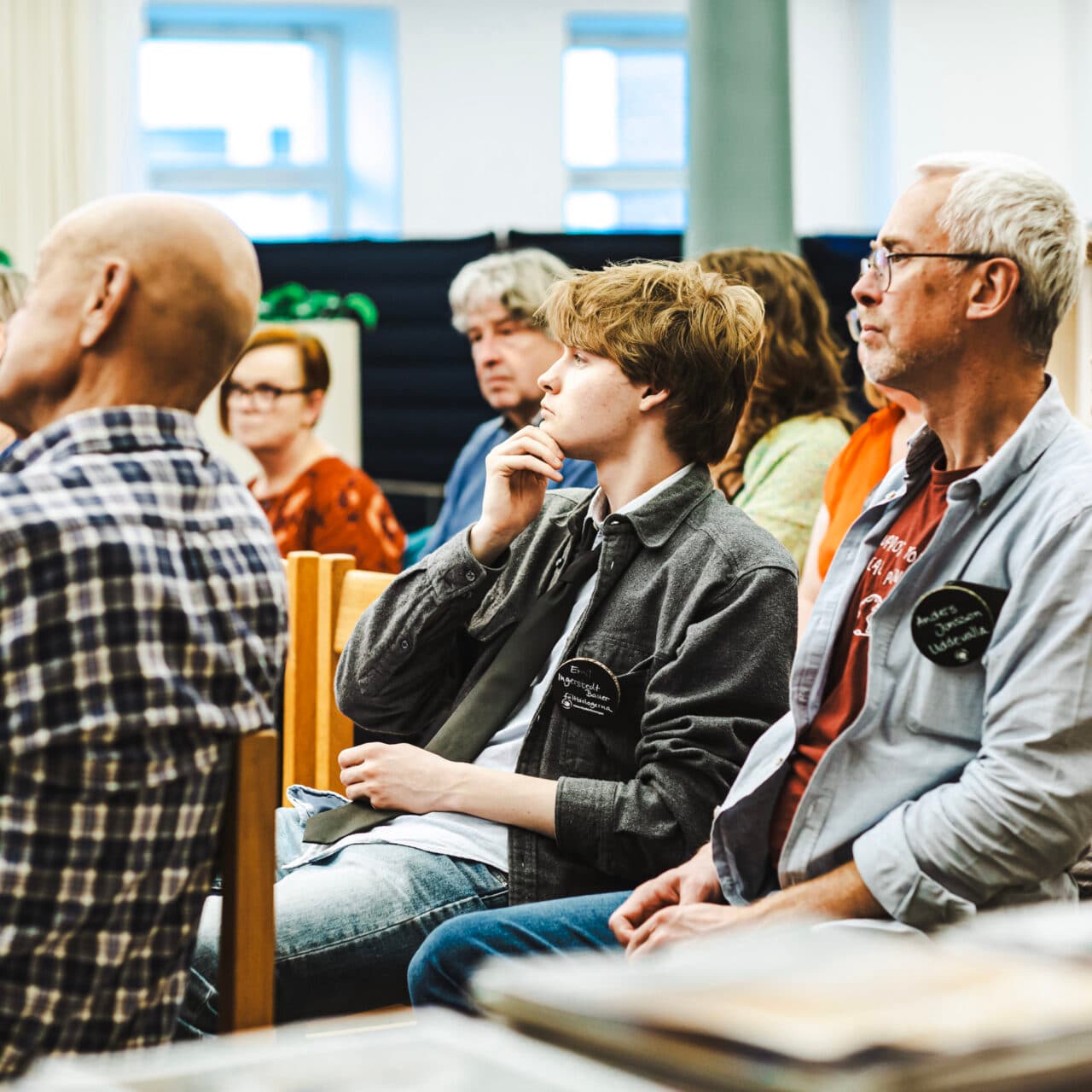 Bilden visar en grupp människor som sitter på stolar och verkar vara fokuserade på något som pågår ...